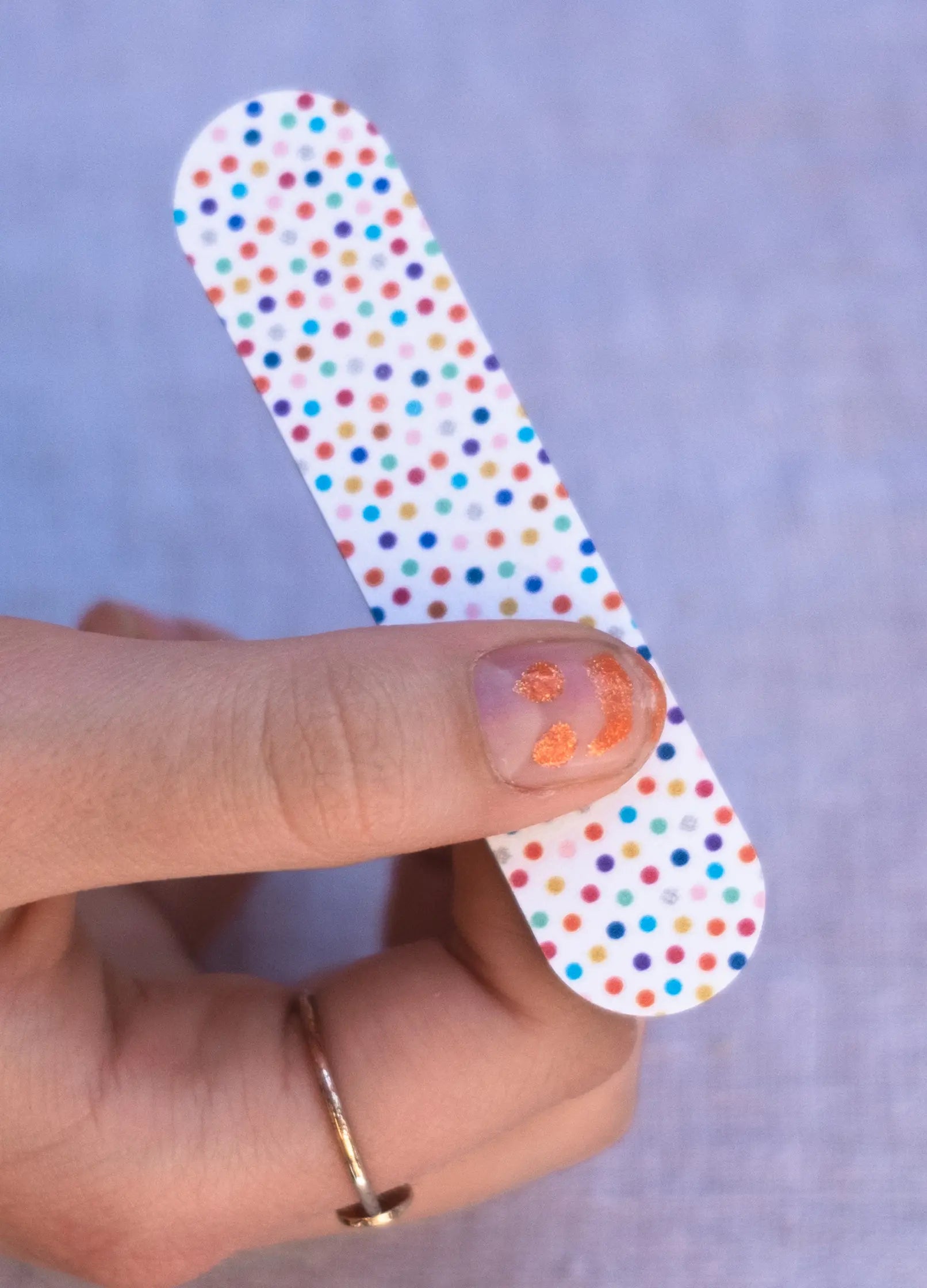 Ręka z pomalowanym pomarańczowym lakierem na paznokciu i kolorową polką pilniczkiem do paznokci odklejalny lakier do paznokci dla dzieci